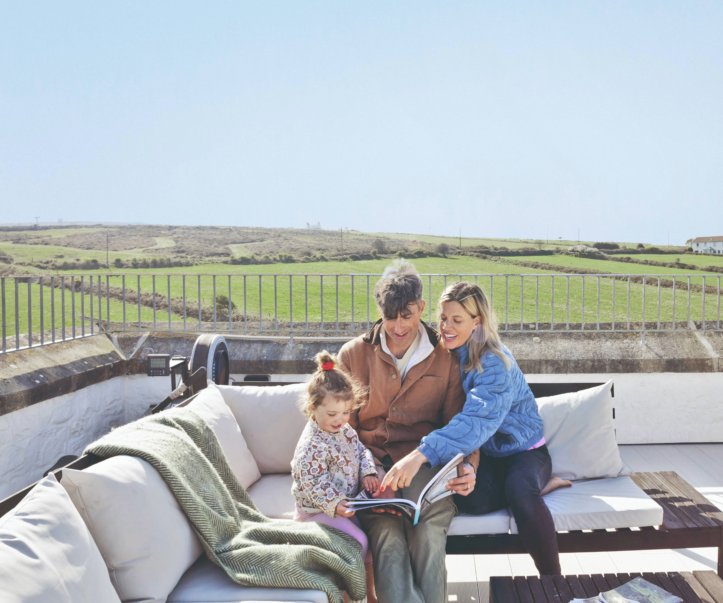 The homeowners and child sitting on outdoor furniture with view of fields in the background