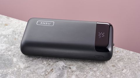 The Iniu PD 22.5w 20000mAh on a stone surface against a pink background