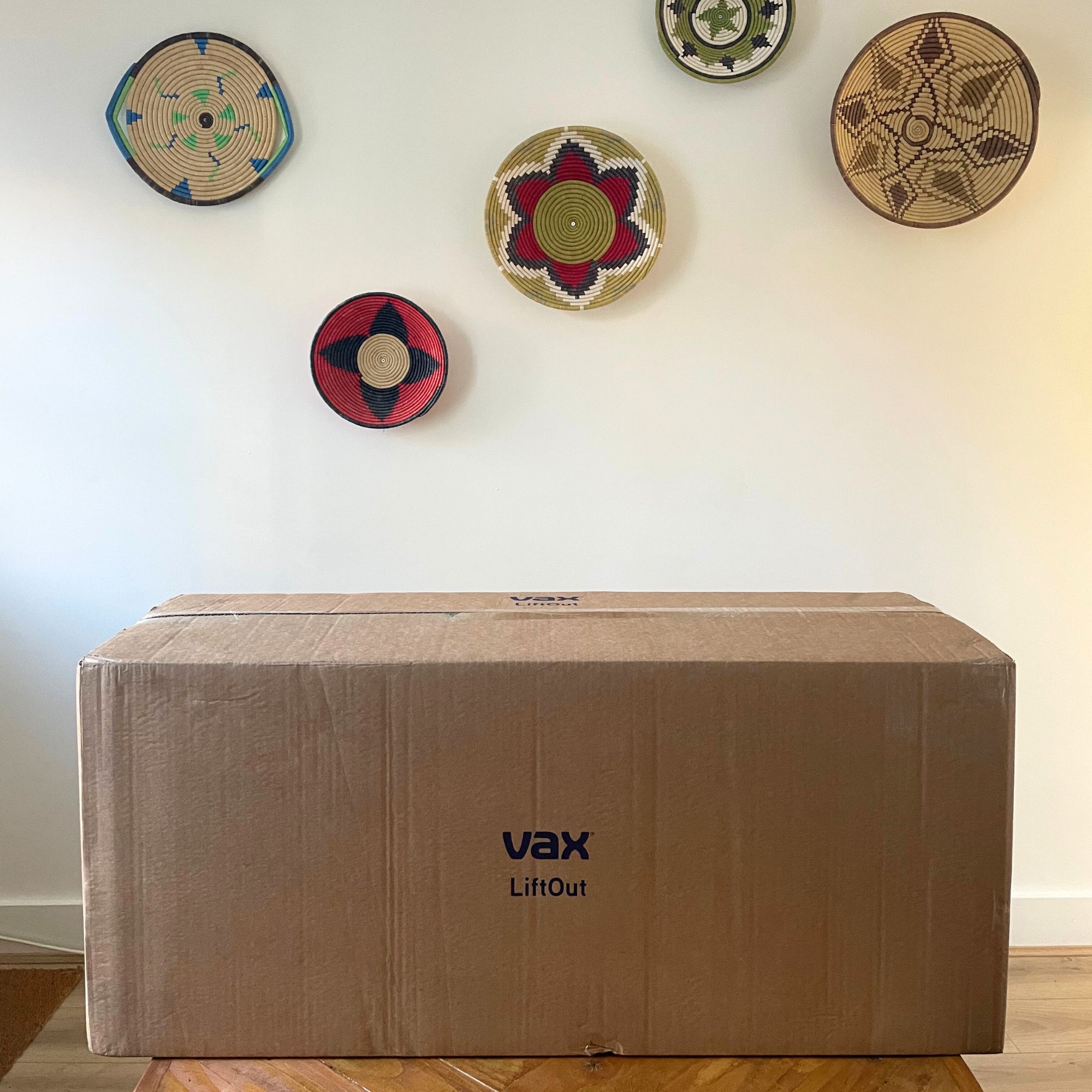 Box of the Vax LiftOut Reach Pet Design Vacuum Cleaner sitting on a table in front of a white wall with colourful baskets on it