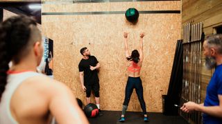 Woman performs wall ball exercise while three people look on