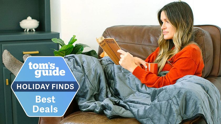 A woman reads a book while covered in the Layla Weighted Blanket. A holiday deals badge is in the left-hand corner.