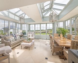 Harwood orangery with rattan dining chairs, a wooden table, and a cream sofa set with a tiled floor