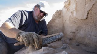 A man brushes sand off the remnants of a prehistoric campsite in New Mexico.