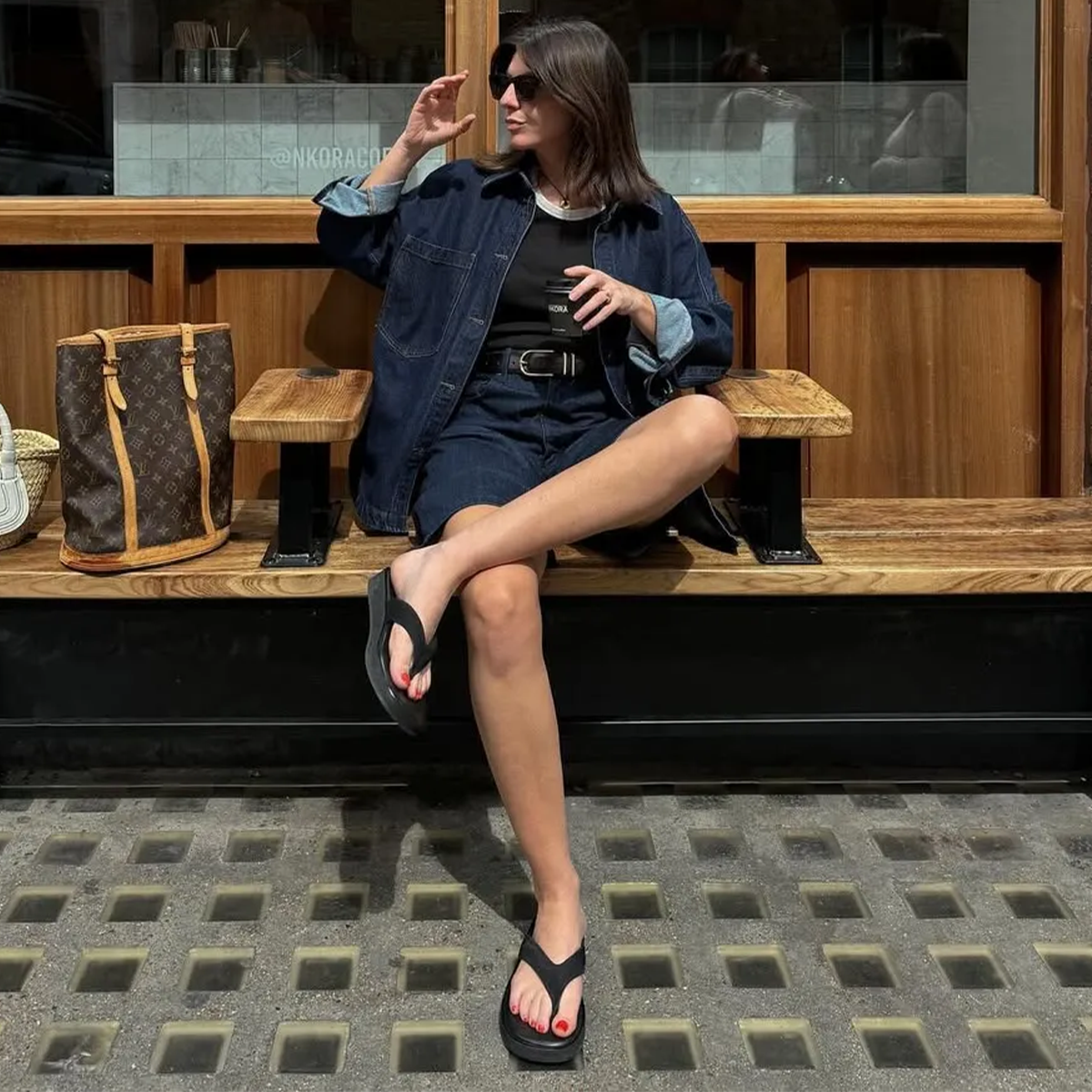 Woman wearing spring flip flop outfit with denim jacket, denim shorts, black sweater and black flip flops.