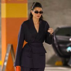 Kendall Jenner styles an orange Bottega Veneta bag with a navy suit and sunglasses.