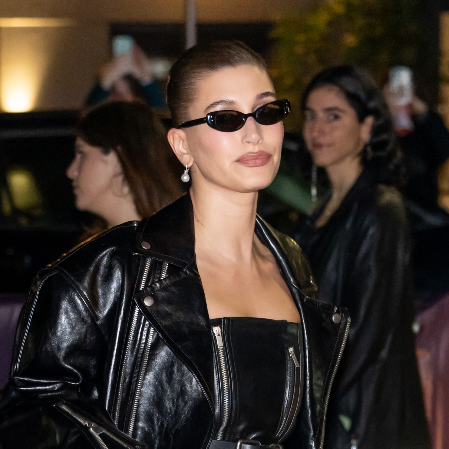 a paparazzi photo of a white woman wearing a black leather jacket, black sunglasses, and a slick bun