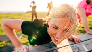 Close-up of woman's smiling face as she attempts an incline push-up on a bench outside