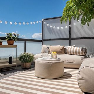 Bright outdoor rooftop/appartment space with white outdoor couches, center table and shelving