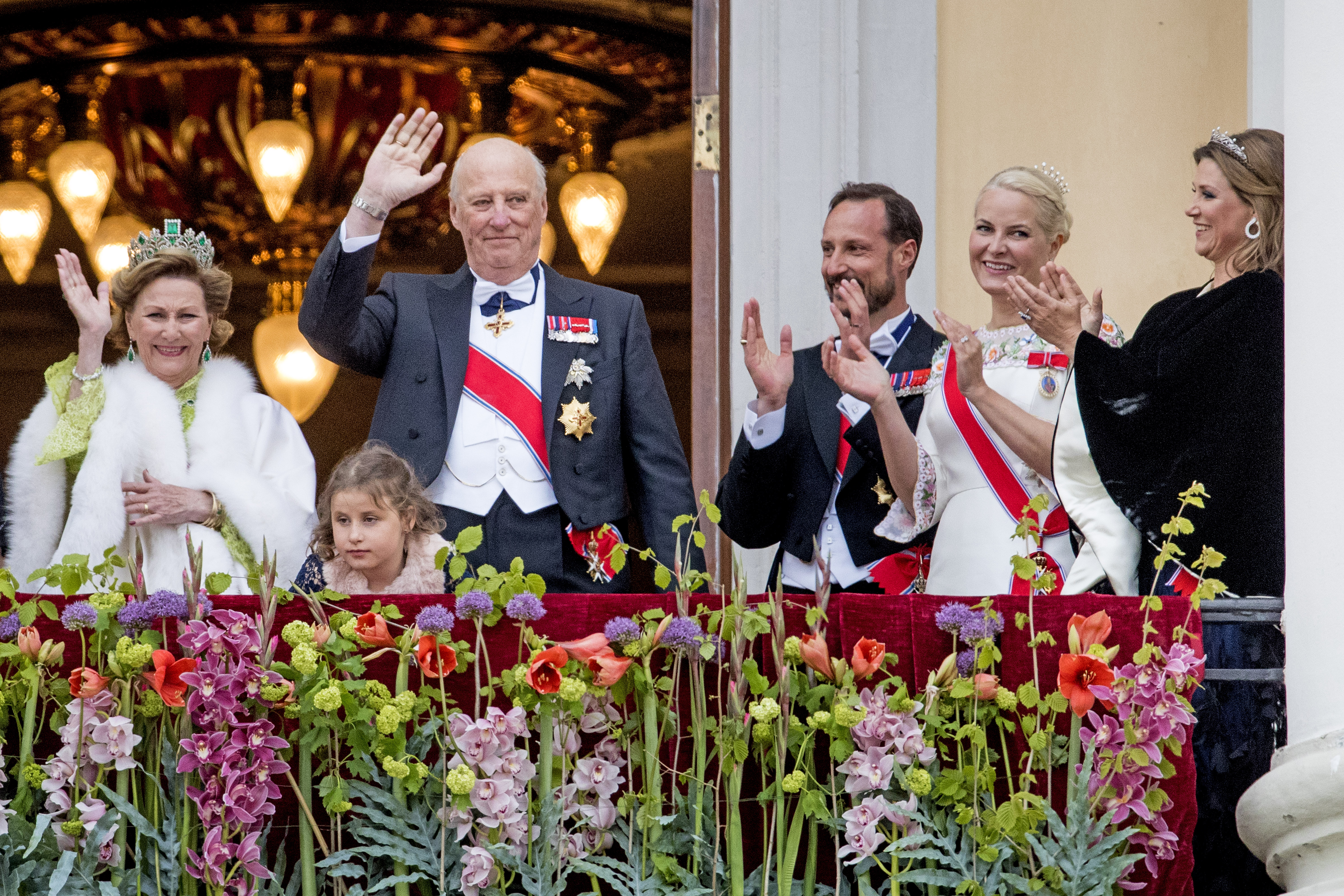 Members of the Norwegian royal family clapping on a balcony as King Harald waves