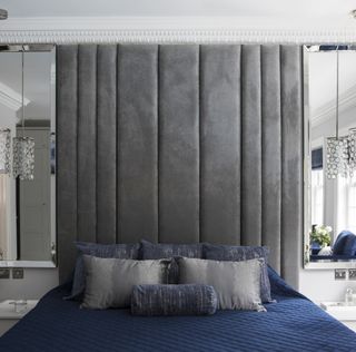 Double bed with full-height gray velvet headboard and mirrors on each side