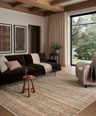 Neutral living room with wood beams, velvet brown sofa, large woven rug and boucle armchair and small wood side table