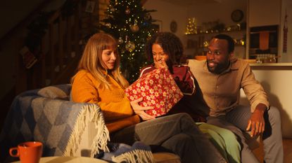 three people sat on sofa giving Christmas gifts