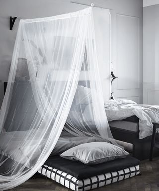 A black and white monochrome bedroom with mattress on floor decorated with a voile canopy hung via shelf bracket