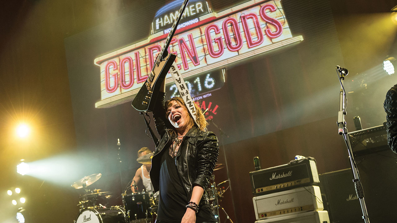 A photograph of Lzzy Hale raising her guitar onstage at the Golden God Awards