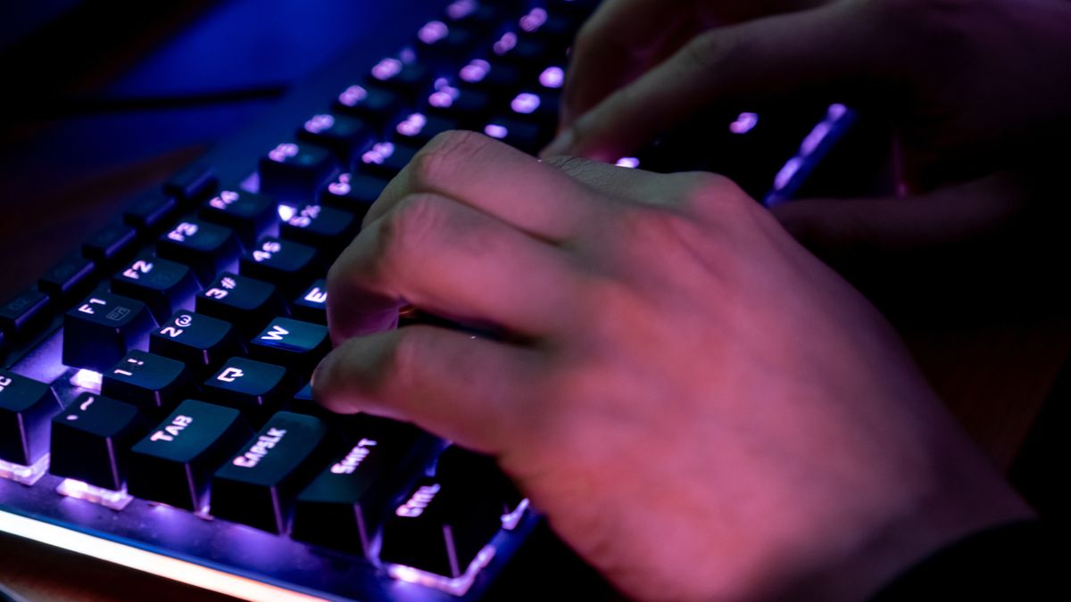 A person typing on a keyboard which has purple backlighting under the keys