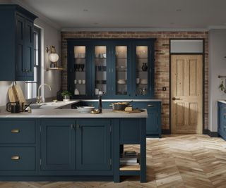 A kitchen with indigo cabinets, wood flooring, white countertops, and brick walls