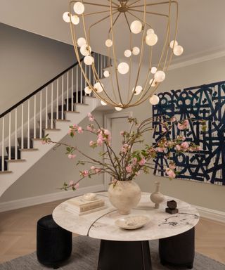 A large entryway with a sculptural light fixture, marble round table, and black and white piece of artwork on the wall