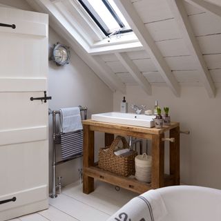 bathroom with white wall sloping roof and white wash basin on wooden table