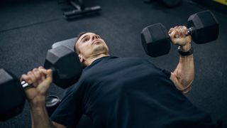 Man performs dumbbell bench press in gym