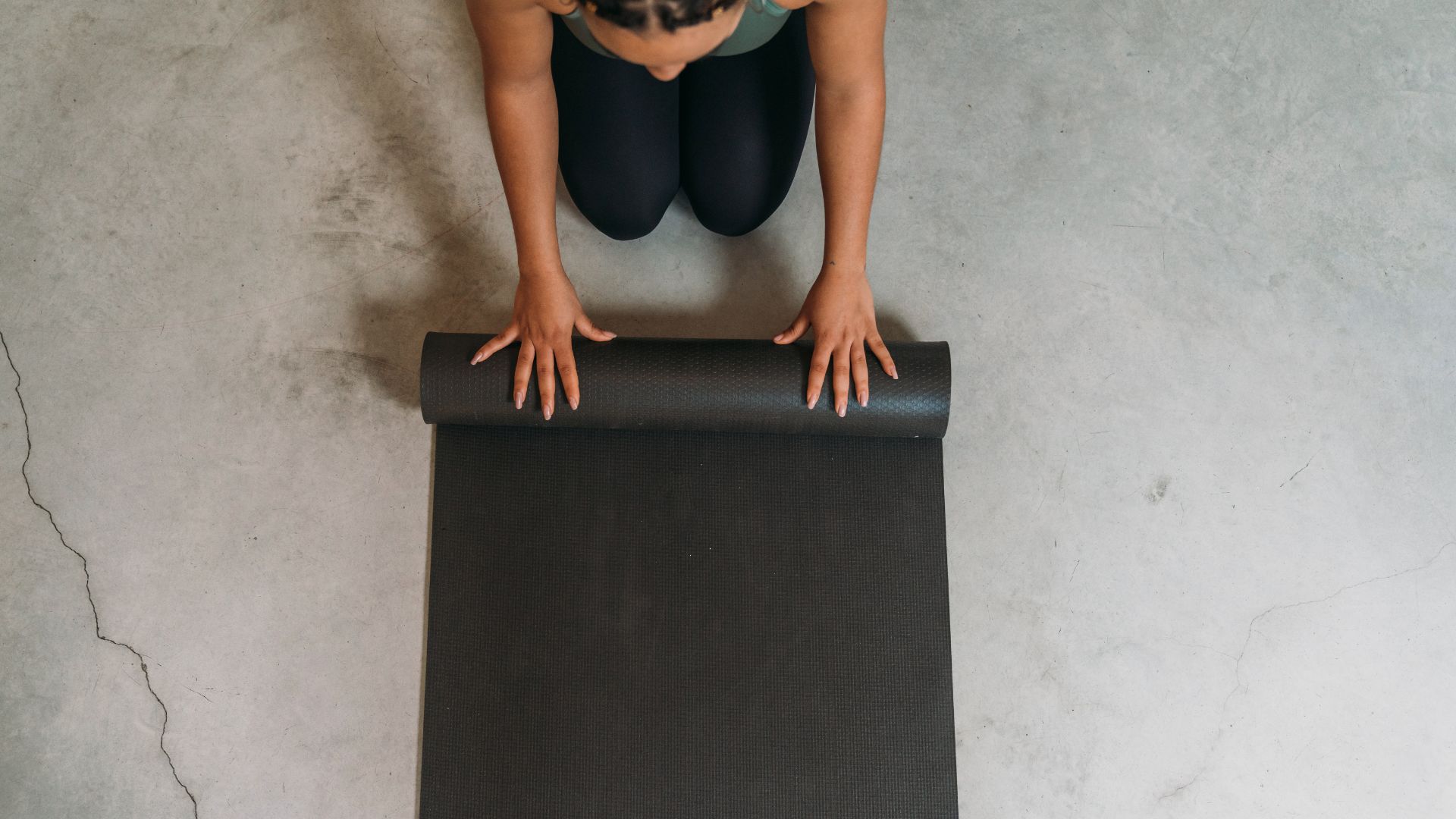 Woman rolling out yoga mat to do frog stretch on the floor