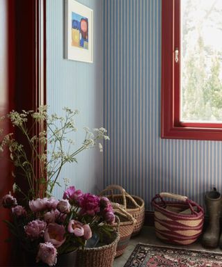 boot room with blue and white striped wallpaper, red window frame and woven baskets on the floor with pink flowers