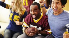 A woman and two men celebrate while watching a football game at home.