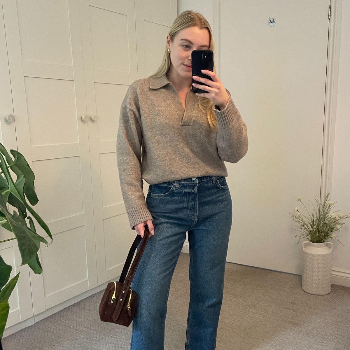 Woman wears beige jumper, blue jeans and brown handbag