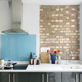 A kitchen with exposed brisk wall, blue splashback, chrome extractor and sink