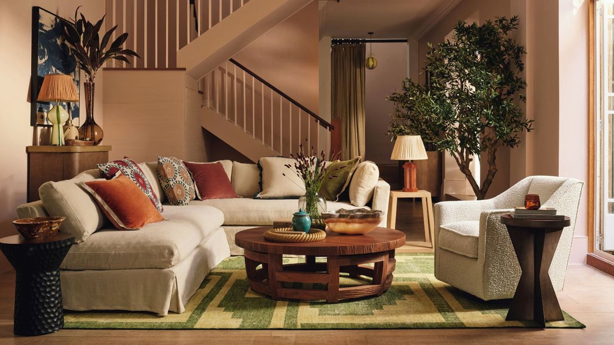 A warm living room with a neutral L-shaped sofa, patterned cushions, and a round wooden coffee table on a green rug. Soft lighting, natural textures, and earthy tones create a cosy feel.