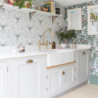 Utility room with white cabinetry, patterned wallpaper, brass hardware and belfast sink