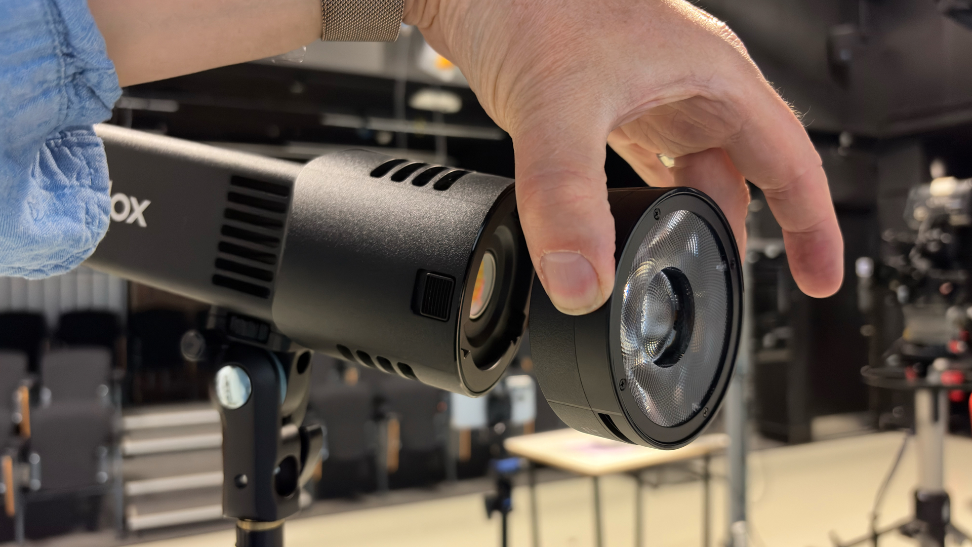 Side shot of a hand attaching the supplied reflector to the flashlight-shaped Godox RS100Bi, which is mounted on a lighting stand in a studio.