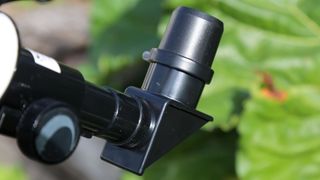 The right-angle of a black telescope eyepiece is seen in front of a blurry green-leaf background.