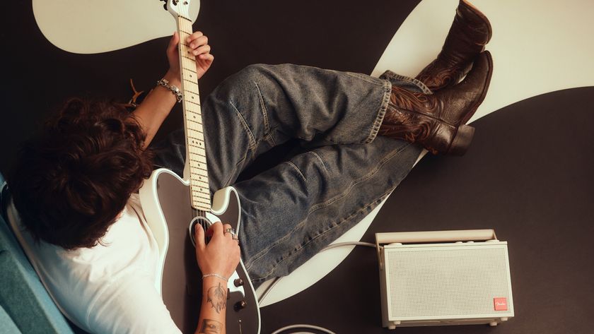 A young man sitting down playing an electric guitar plugged into a Fender Audio ELIE portable speaker.