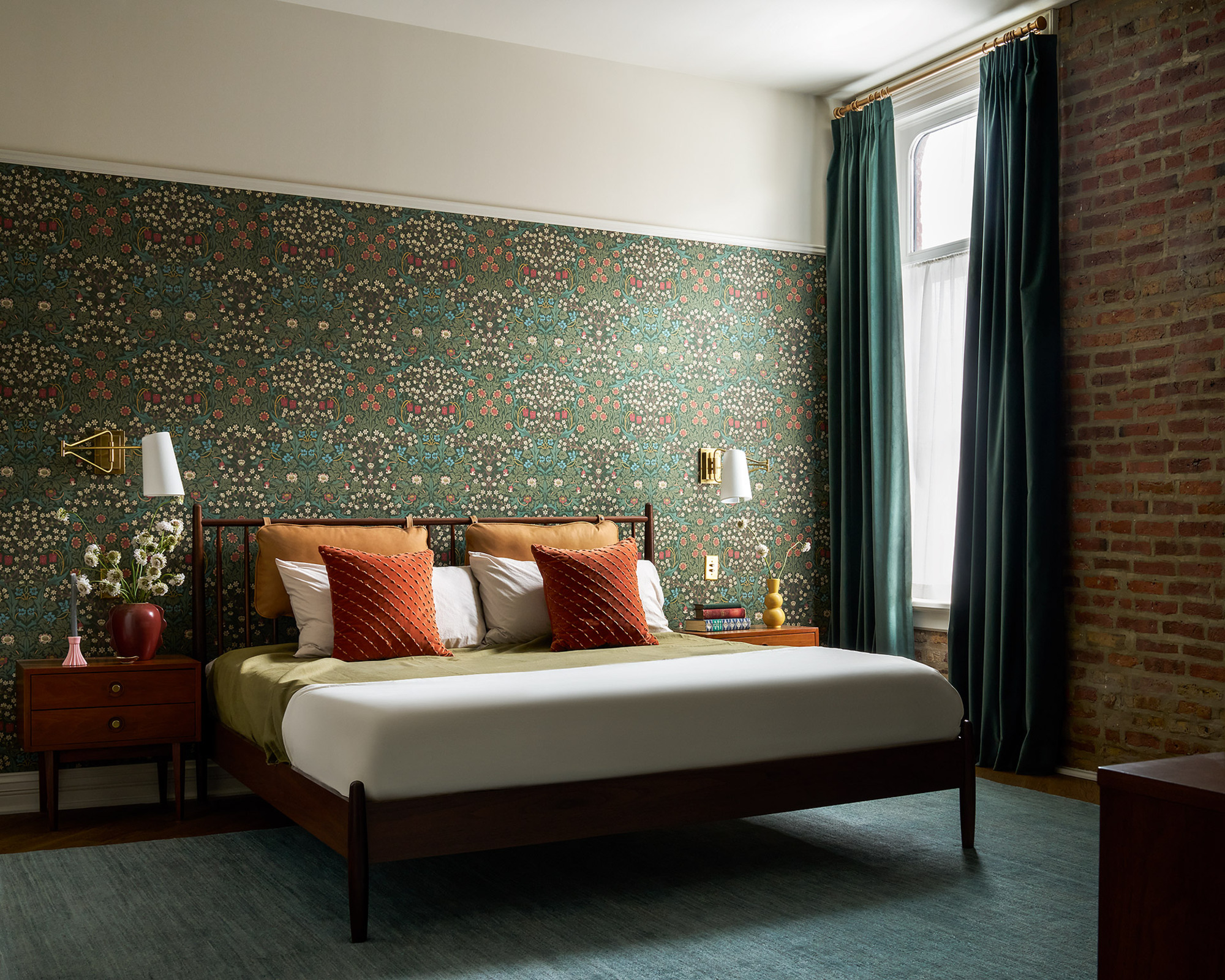 green patterned wall with a bare brick. The bed in the middle of the room includes burnt orange cushions and green curtains