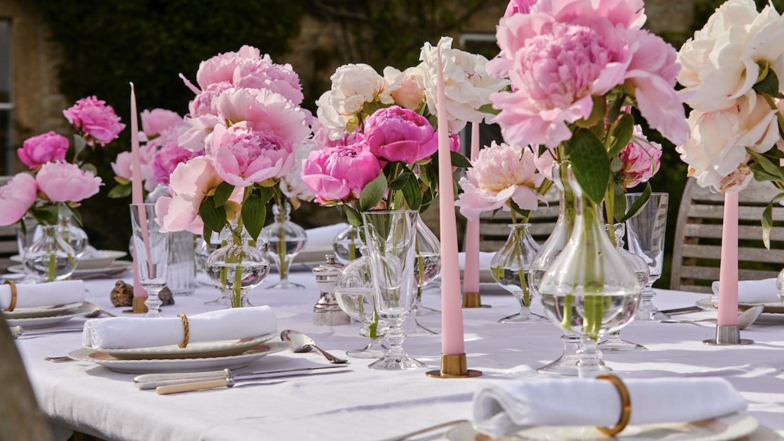 table set with plates and napkins with glass vessels holding lots of pink peonies in the middle