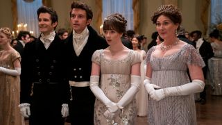 From left to right: Luke Thompson as Benedict Bridgerton, Jonathan Bailey as Anthony Bridgerton, Claudia Jessie as Eloise Bridgerton in a white and silver gown, Ruth Gemmell as Lady Violet Bridgerton. They all look kind of surprised.