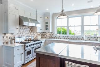 white kitchen cabinets with patterned backsplash, mahogany island with stainless steel top, chrome range and cooker hood