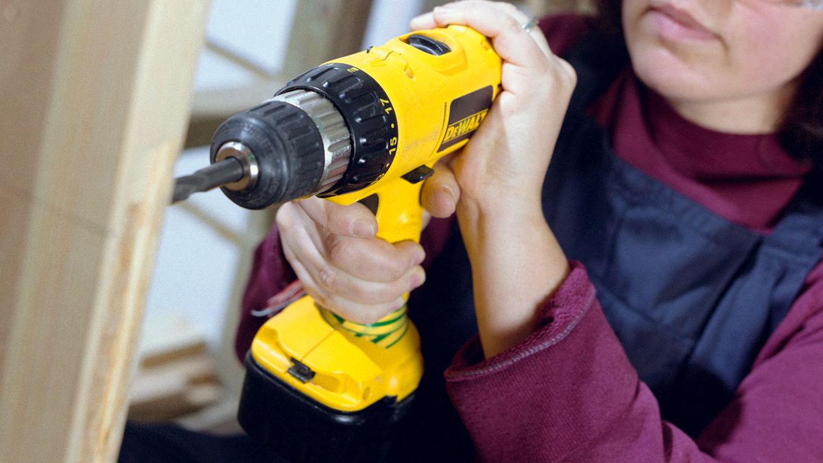 Woman using yellow DeWalt drill to drill into bare wooden door