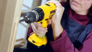 Woman using yellow DeWalt drill to drill into bare wooden door