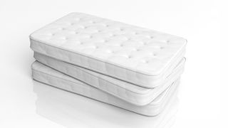 Image shows three clean white mattresses without fiberglass stacked on top of one another on a glossy white floor