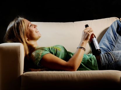 A woman relaxing on a sofa with a bottle of beer in hand