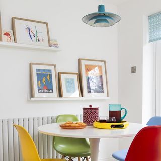white dinning table with colourful chairs white wall and frames on wall