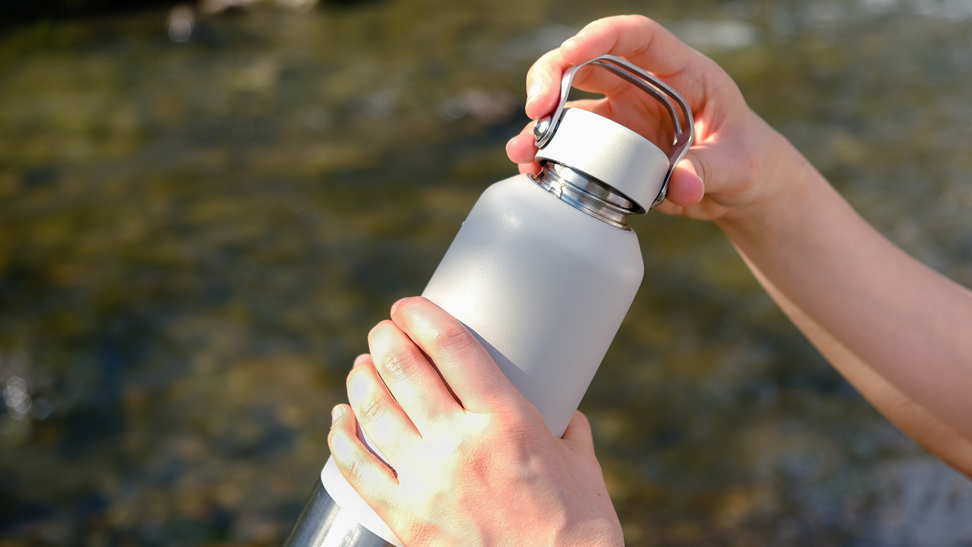 Person in front of a stream putting the lid on a reusable water bottle