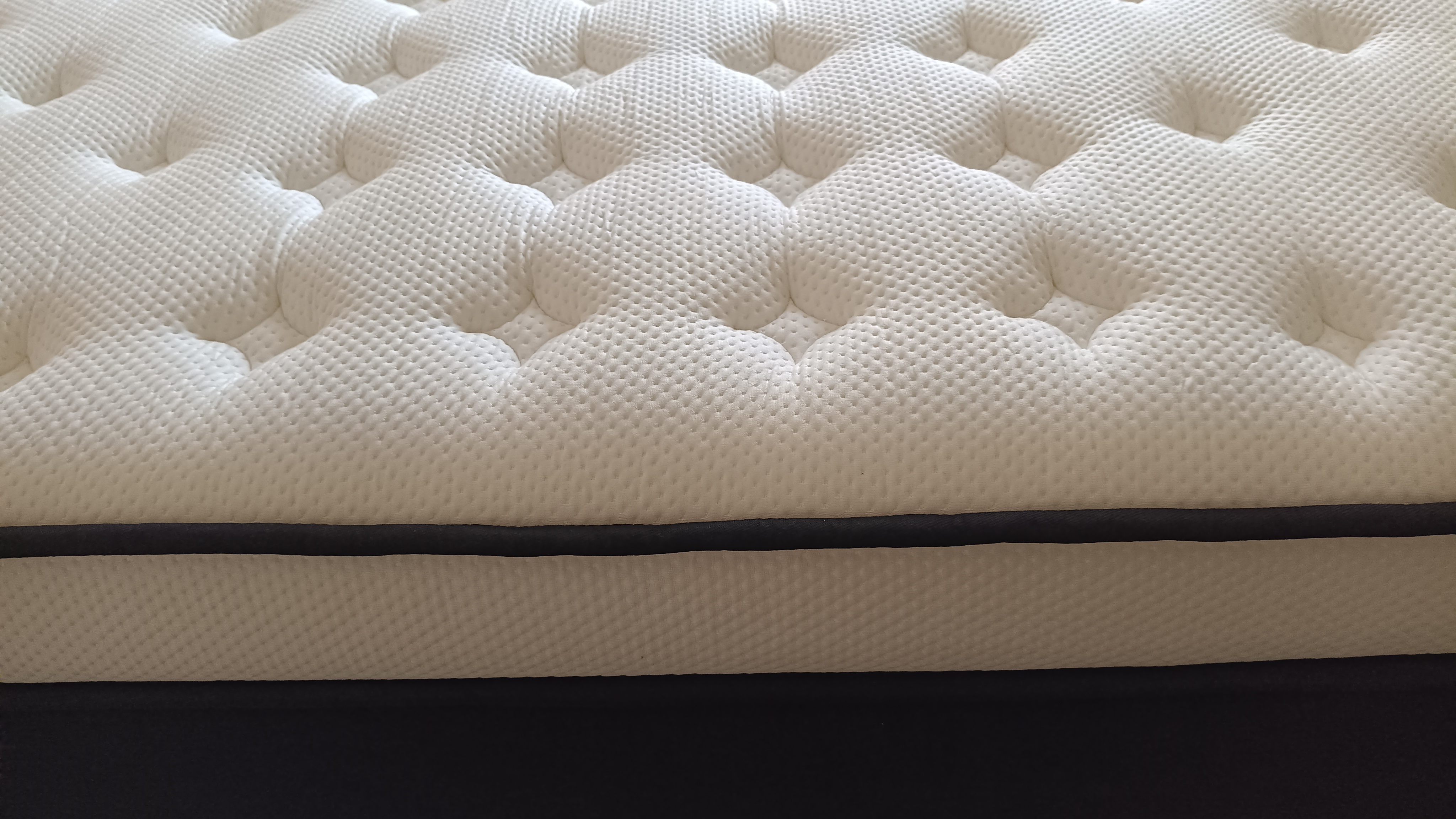 A tight shot of the mattress edge displays the contrast between the plush white topper, the black piping, and the sturdy dark fabric side walls.