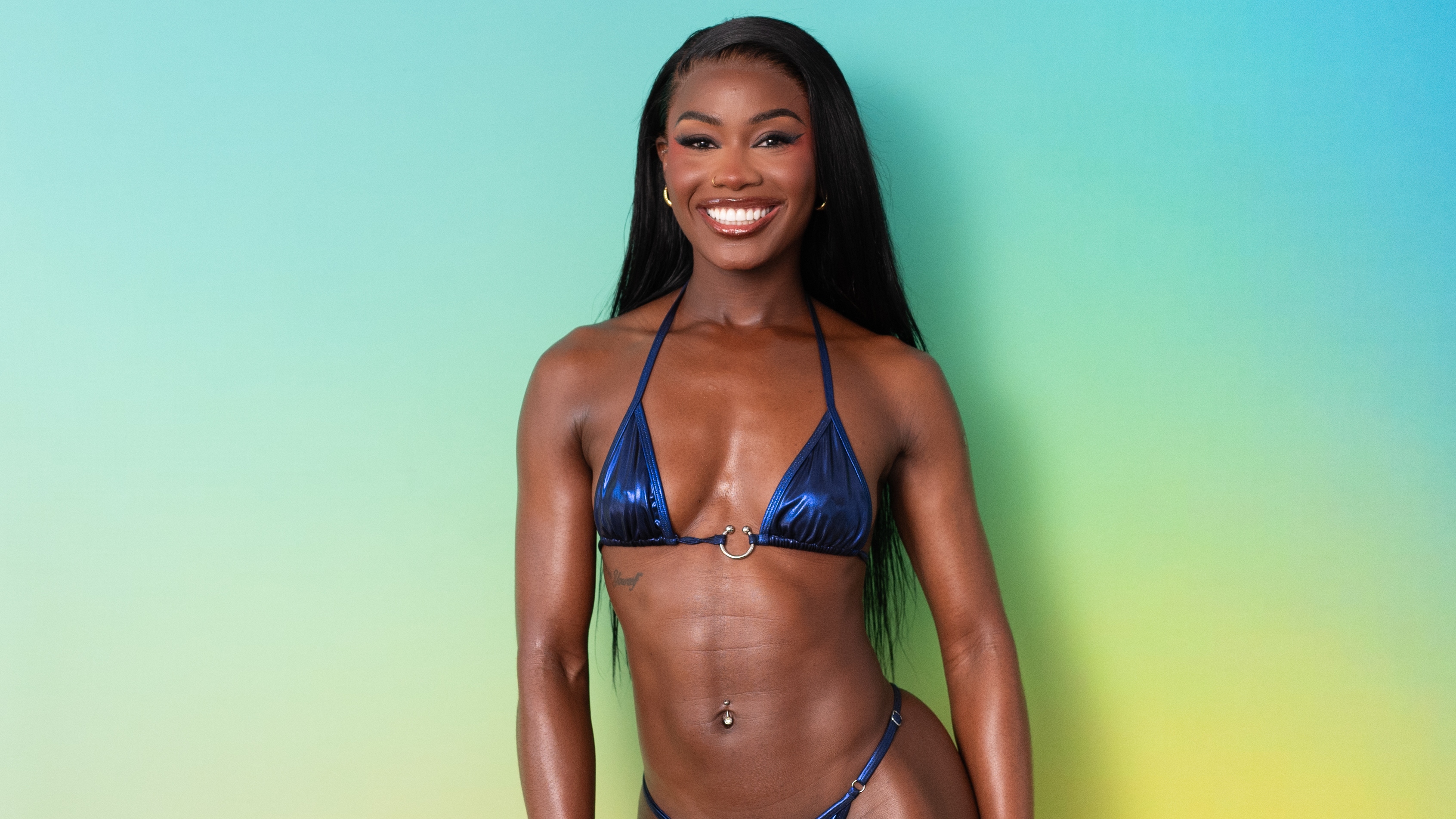 Bombshell Billykiss standing in front of a green background in swimwear