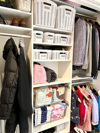 Closet interior with coat rails, shoe storage and ehitr baskets lining shelves with clothes inside