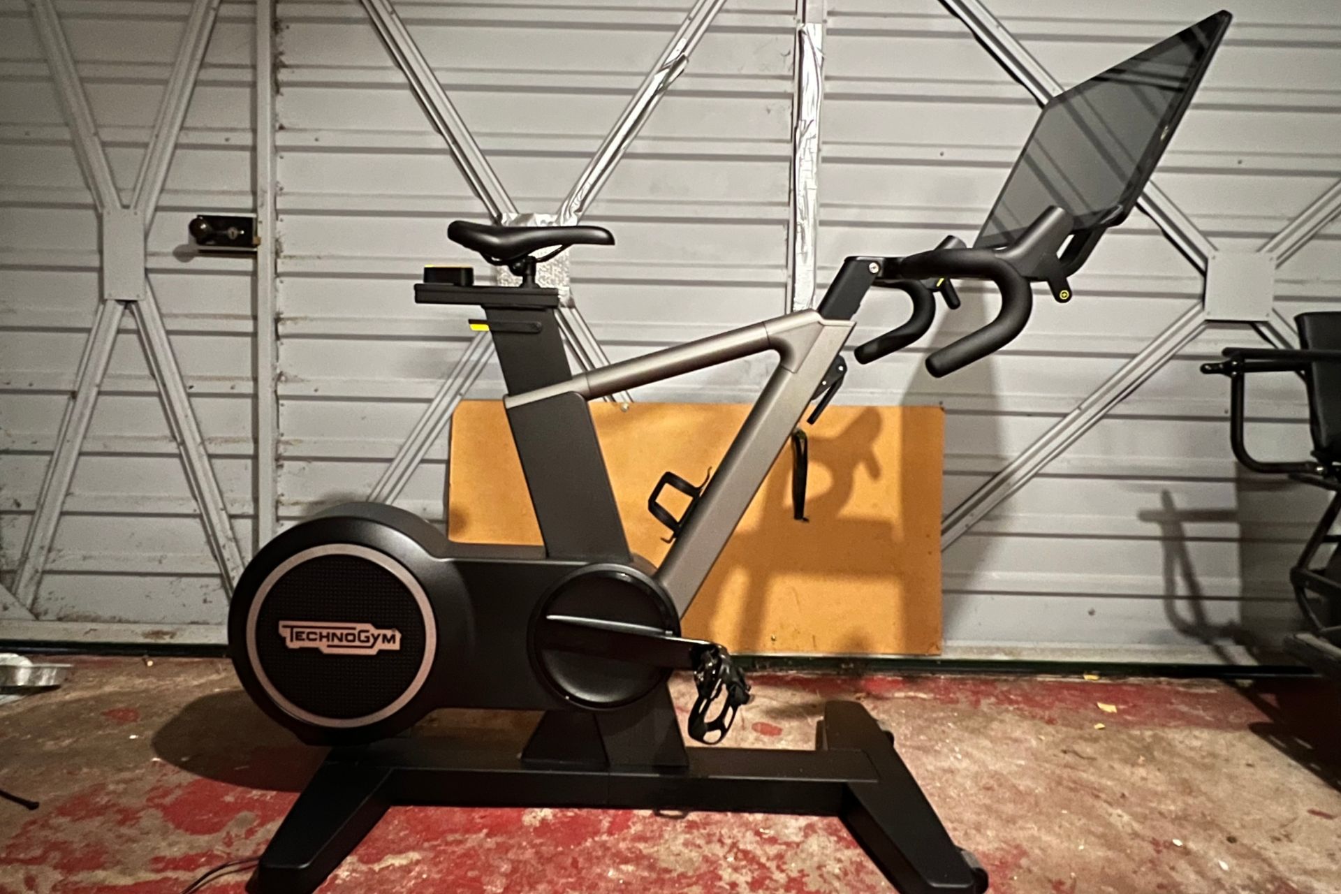 The TechnoGym Ride bike comes with an intergrated screen and dropped handlebars. This image shows the bike with a grey garage door in the background.