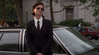Linda Fiorentino smiles in a suit, standing next to a car in Men in Black.