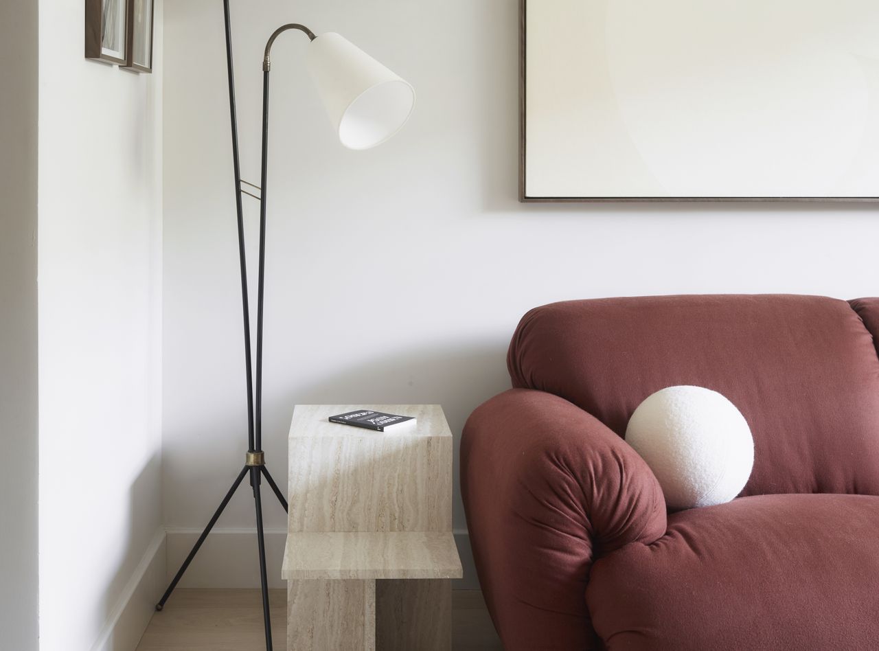 A living room with white walls, a red sofa, and a floor lamp