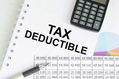 Text Tax Deduction on a notepad among charts and reports on the table.